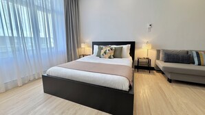 Une chambre d’hôtel moderne avec un grand lit, un canapé, deux tables de chevet avec des lampes et des rideaux légers.