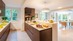 A modern kitchen with a central island, large windows, and a dining area with wicker chairs.