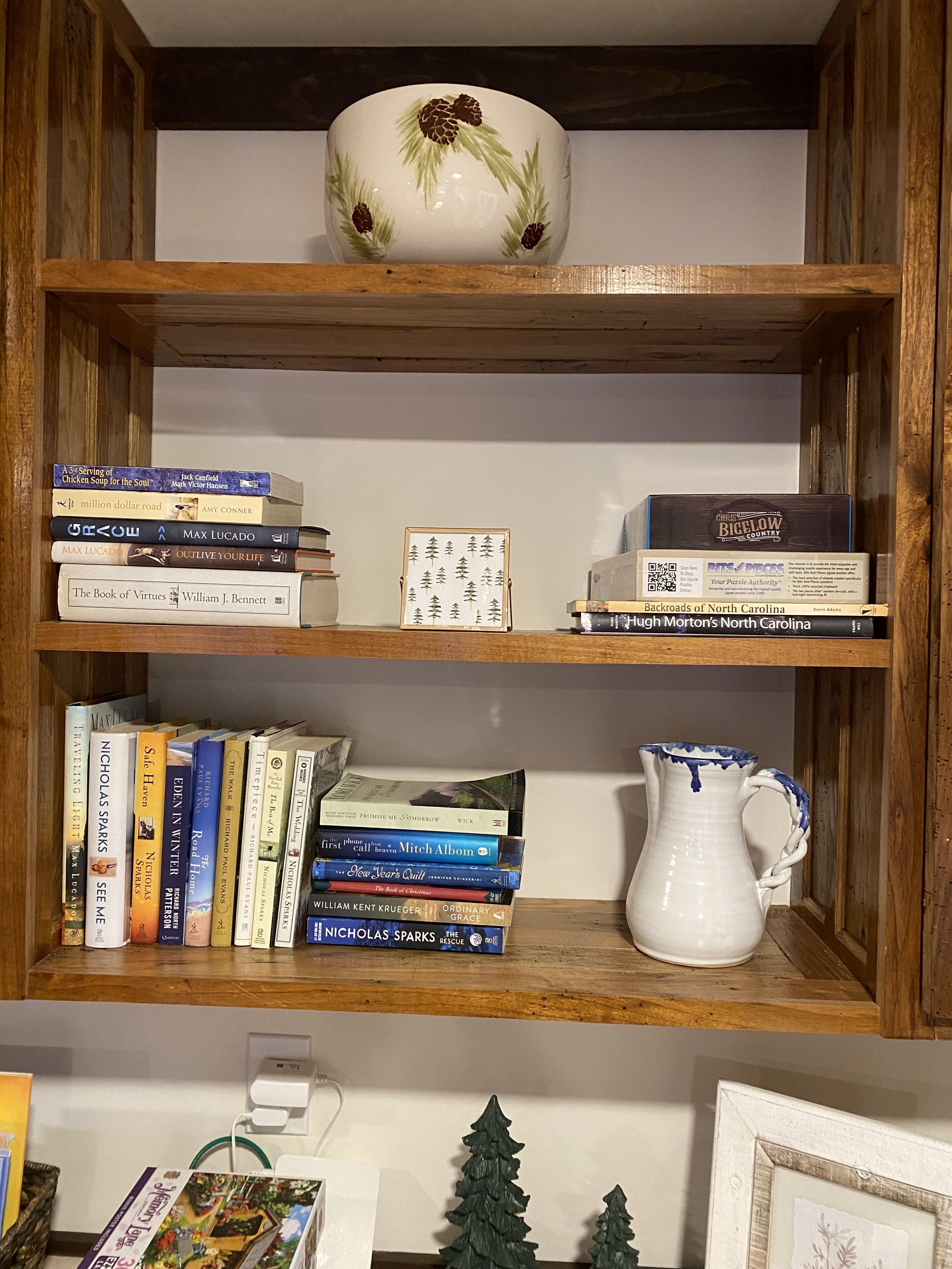 A wooden bookshelf with books and a white ceramic pitcher.
