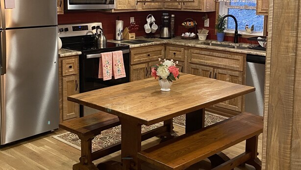Une cuisine avec des meubles de rangement en bois, un réfrigérateur en acier inoxydable, un four à micro-ondes, une cuisinière et une table à manger en bois accompagnée d’un banc.