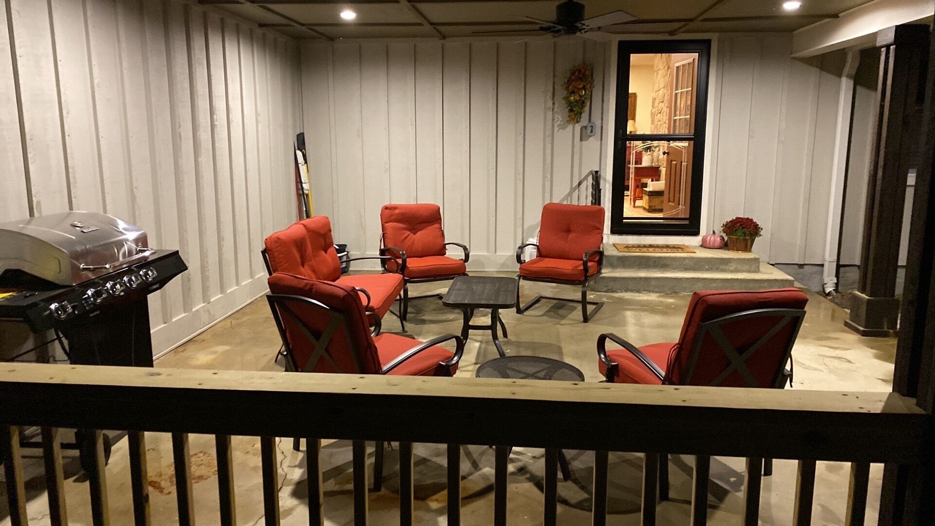 Un patio cubierto con cuatro sillas rojas, una mesa redonda pequeña y una parrilla de barbacoa.