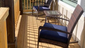 Un espace extérieur abrité doté d’une terrasse en bois, de deux fauteuils à bascule en osier avec des coussins bleus et d’une table en verre.