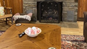 Un salon chaleureux avec une cheminée en pierre, un téléviseur à écran plat fixé au-dessus, et une table basse en bois agrémentée d’objets décoratifs.