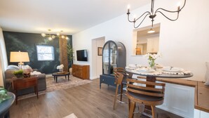 Un salon moderne avec un mur de couleur sombre, une table à manger en bois avec des chaises, un téléviseur fixé au mur et un lustre.