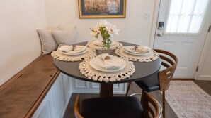 Une table à manger dressée pour quatre personnes, avec de l’argenterie blanche, un vase rempli de fleurs blanches et des coussins à rayures sur un banc.
