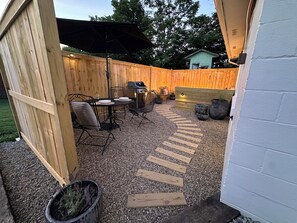 Eine Terrasse mit Holzzaun, Grill und Sitzgelegenheit mit Stühlen und Tisch.