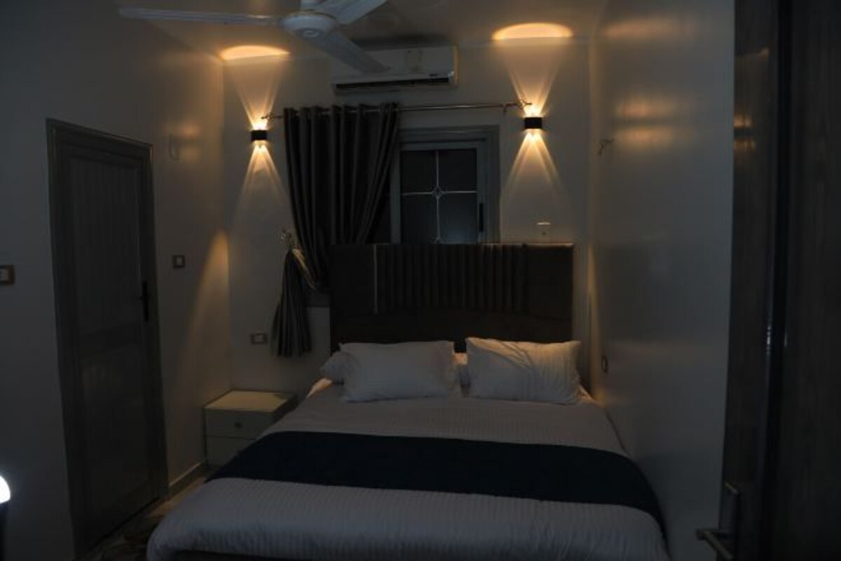 A bedroom with a bed, bedside tables, a window with curtains, and an air conditioning unit.
