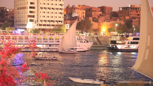 A waterfront scene with a sailboat, a large building, and a bridge. - crystala guest house (Aswan)