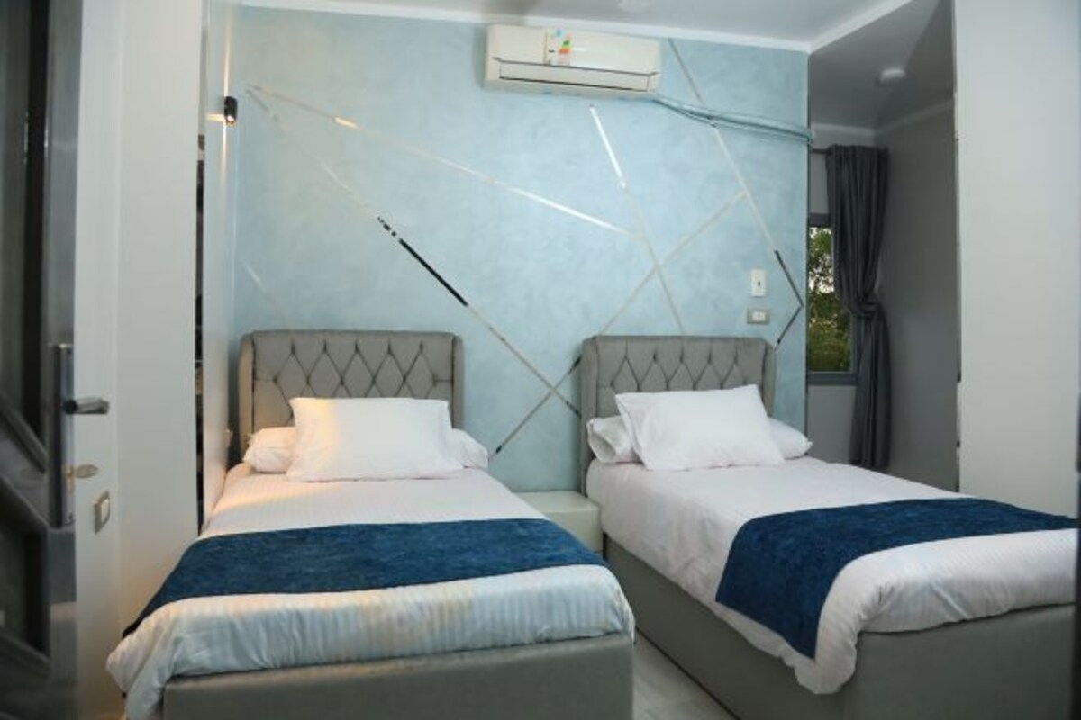 A hotel room with two beds, a wall-mounted air conditioner, and a window with curtains.