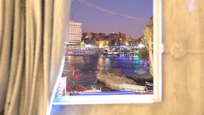A framed photograph of a river scene with boats, buildings, and a rocky shore. - crystala guest house (Aswan)
