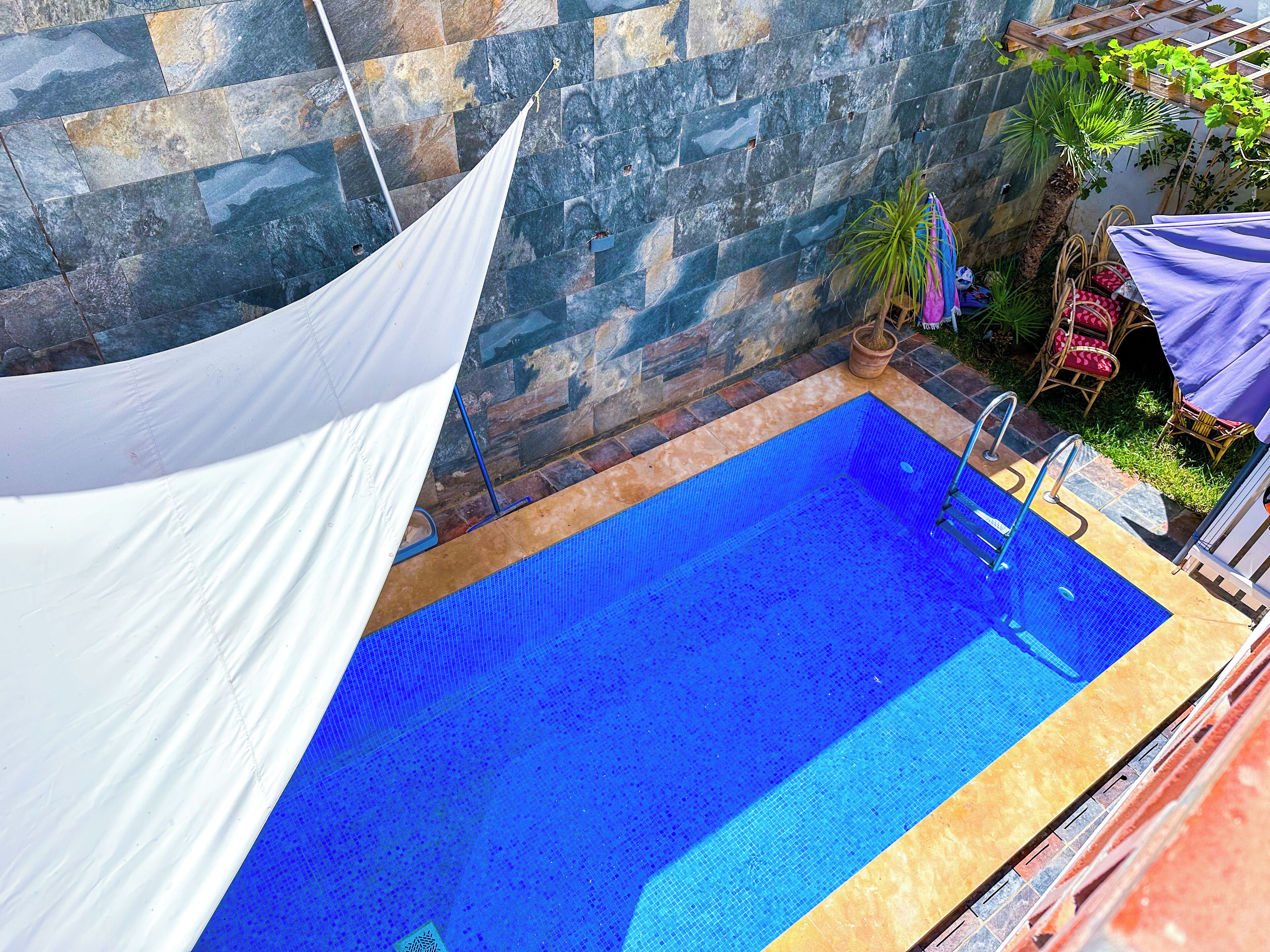 Una piscina amb un voreig enrajolat, una tenda blanca i una paret de pedra al fons.