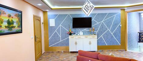 A living room with a sofa, a television mounted on the wall, and a cabinet with drawers.