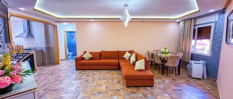 A modern living room with a sectional sofa, a dining area, and a kitchen with a gas stove.