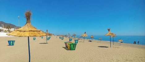 A beach with thatched umbrellas and sun loungers.