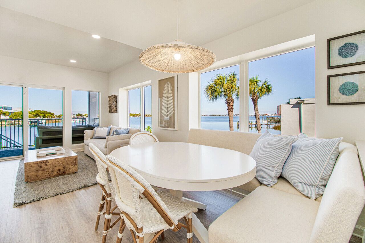 A spacious living room with a round white table, comfortable seating, large windows, and a view of the sea.