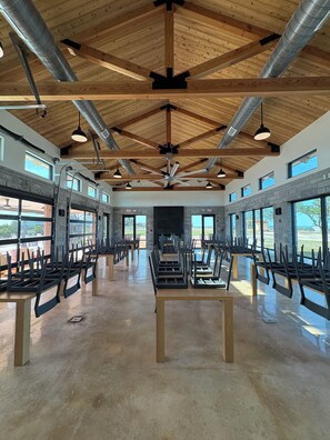 A spacious interior with high ceilings, exposed wooden beams, and large windows offering views of the outdoors.