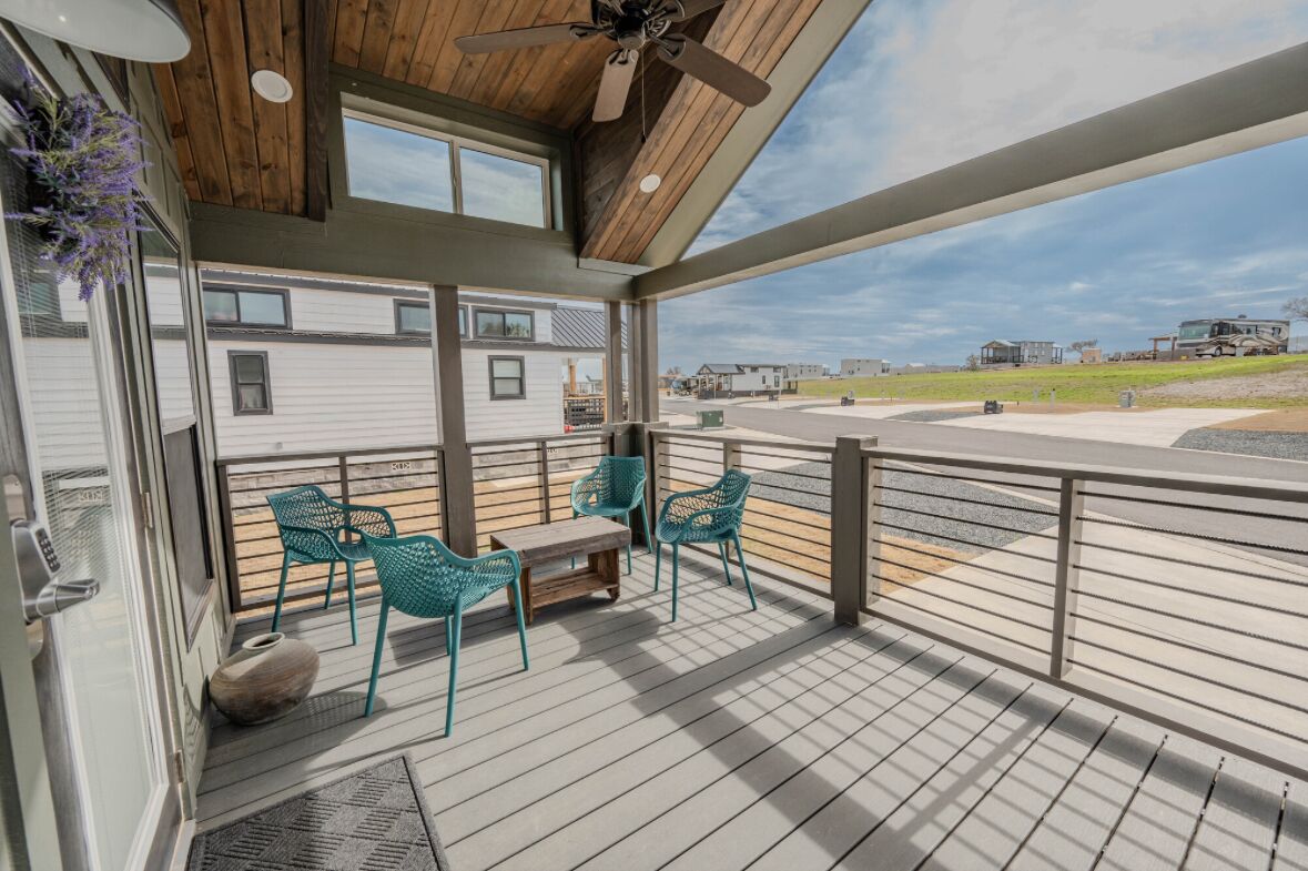 Une terrasse extérieure couverte, dotée d’un plancher en bois, de chaises vertes et d’un ventilateur de plafond.