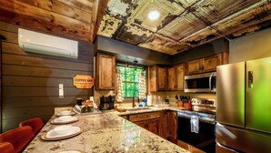 A kitchen with wooden cabinets, a granite countertop, stainless steel appliances, and a coffee bar sign. - NOT YOUR GRANDMA’S CABIN! King Loft, WIFI, Game Room, Hot Tub & Fire Pit! (Almond)