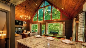 A spacious kitchen with a large island, wooden ceiling, and large windows offering a view of the outdoors. - NOT YOUR GRANDMA’S CABIN! King Loft, WIFI, Game Room, Hot Tub & Fire Pit! (Almond)