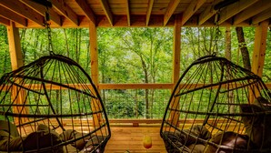 Two wicker chairs facing each other with a wooden table between them, a glass of drink, and a book on the table. - NOT YOUR GRANDMA’S CABIN! King Loft, WIFI, Game Room, Hot Tub & Fire Pit! (Almond)