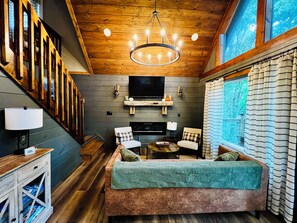 A cozy living room with a fireplace, a television, and a staircase. - "NOT YOUR GRANDMA’S CABIN" King Loft, Starlink, Game Room, Hot Tub & Fire Pit! (Almond)