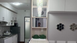 A modern kitchen with white cabinets, a built-in oven, and a microwave. There is a dining area with a wooden table and two purple bar stools. A brown sofa with a red pillow is in the living room area. - 1 Br condo T2-8H (Cagayan de Oro)