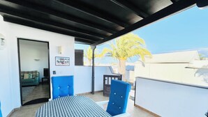 A balcony with a checkered table and blue chairs, a sofa, and a framed picture on the wall. - Trinity House (Costa Teguise)