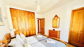 A bedroom with two beds, wooden wardrobes, a dresser, and a mirror. - Trinity House (Costa Teguise)
