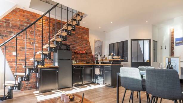 Une cuisine moderne avec un mur en briques, un escalier et un coin repas avec des chaises.