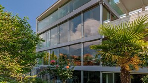 Un edificio moderno con grandes ventanales, un balcón con plantas y un cielo despejado.