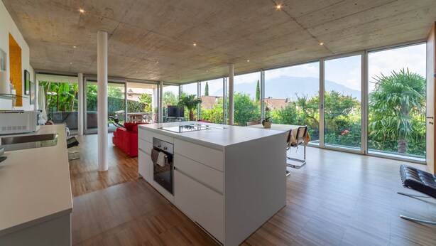Una cocina espaciosa con una isla grande, electrodomésticos modernos y amplias ventanas que ofrecen vistas a zonas verdes y montañas.