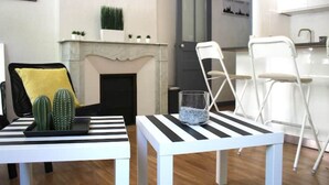 Un salon moderne avec une cheminée, deux tables blanches à rayures noires et une chaise pliante blanche.