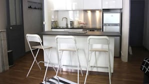 Une cuisine moderne avec des meubles blancs, un plan de travail en acier inoxydable et trois tabourets de bar blancs.