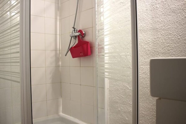 A bathroom with white tiled walls, a shower with a glass door, and a red towel rack.