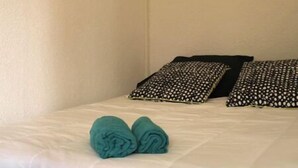 Un lit bien fait, avec une literie blanche et deux serviettes turquoise, des coussins noirs ornés de motifs blancs et un tableau accroché au mur.