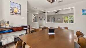 Un vaste espace dédié à la salle à manger, avec une grande table en bois, plusieurs chaises, un ordinateur portable posé sur la table et un lustre au-dessus.