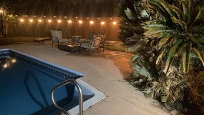 Un jardin avec une piscine, des meubles de patio et des guirlandes lumineuses.