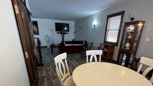 Un coin repas avec une table ronde et quatre chaises, un canapé rouge, un téléviseur et un meuble avec des portes en verre.