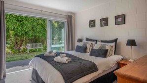 Une chambre avec un grand lit, deux tables de chevet avec des lampes, une vue sur la verdure et un banc dans le jardin.
