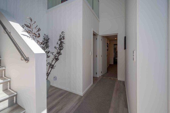 A modern interior with a staircase, a hallway leading to another room, and a decorative wall piece. - Cliffside - Akaroa Holiday Home (Akaroa)