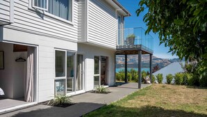 Une maison moderne à deux étages, dotée d’un balcon, d’une terrasse couverte et offrant une vue sur les montagnes et un lac.