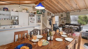 Ein gemütlicher Essbereich mit Holztisch, gedeckt für eine Mahlzeit, eine Küche mit weißen Schränken und ein Wohnbereich mit einer Ledersofa.