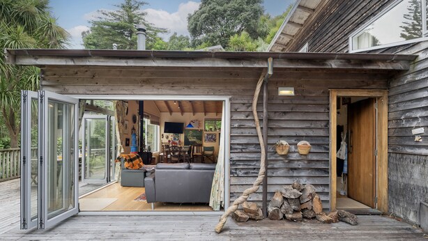 Ein modernes Holzhaus mit einer Glastür, die in ein Wohnzimmer mit Sofa und Essbereich führt.
