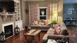 Een woonkamer met een open haard, een plafondventilator, een eethoek en een televisie.