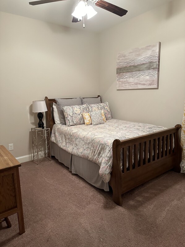 A bedroom with a wooden bed, a nightstand, a lamp, a ceiling fan, and a wall-mounted abstract painting. - Cozy Weekend Rental (Oxford)