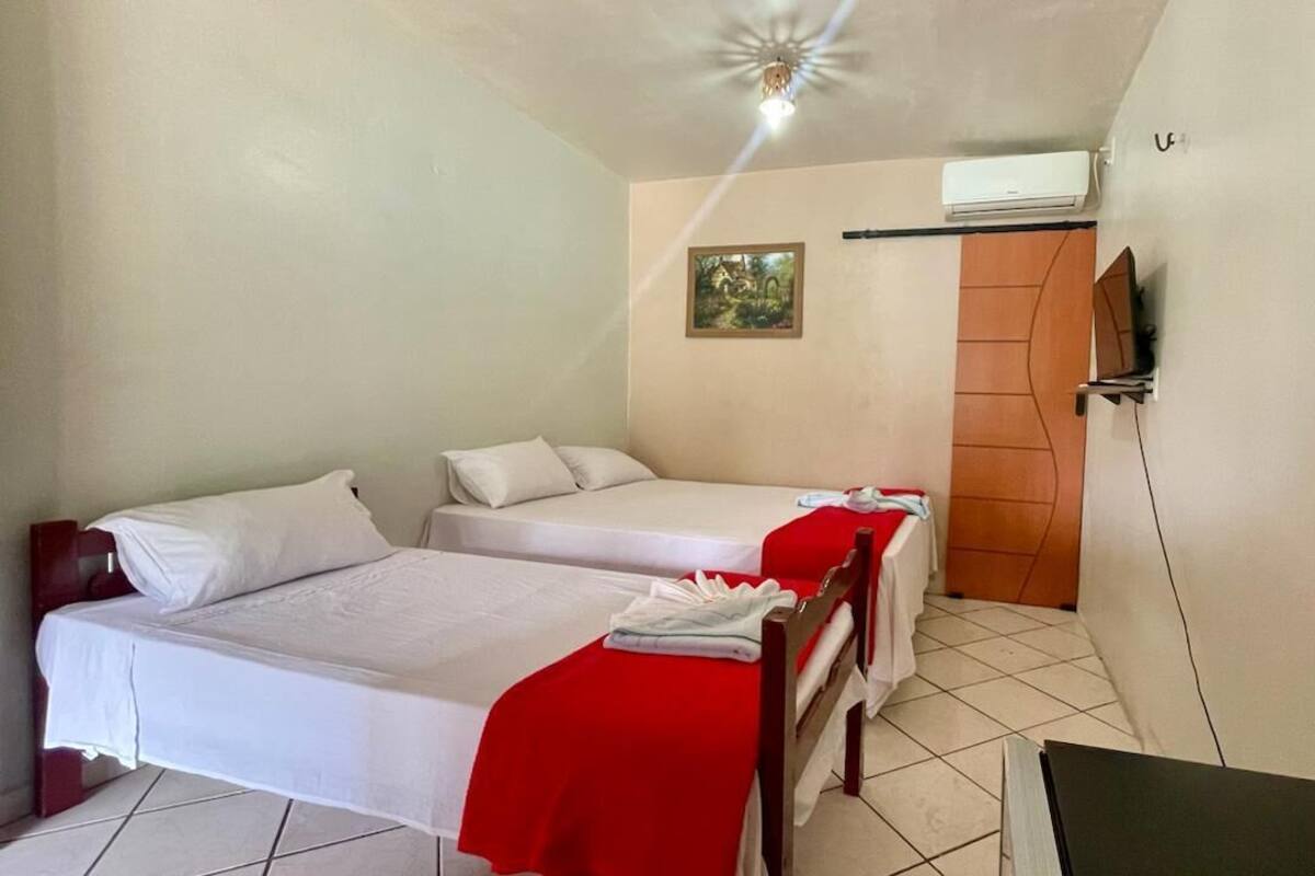 Ein Zimmer mit zwei Einzelbetten, einer Holztür, einem kleinen Tisch und einem an der Wand befestigten Fernseher.