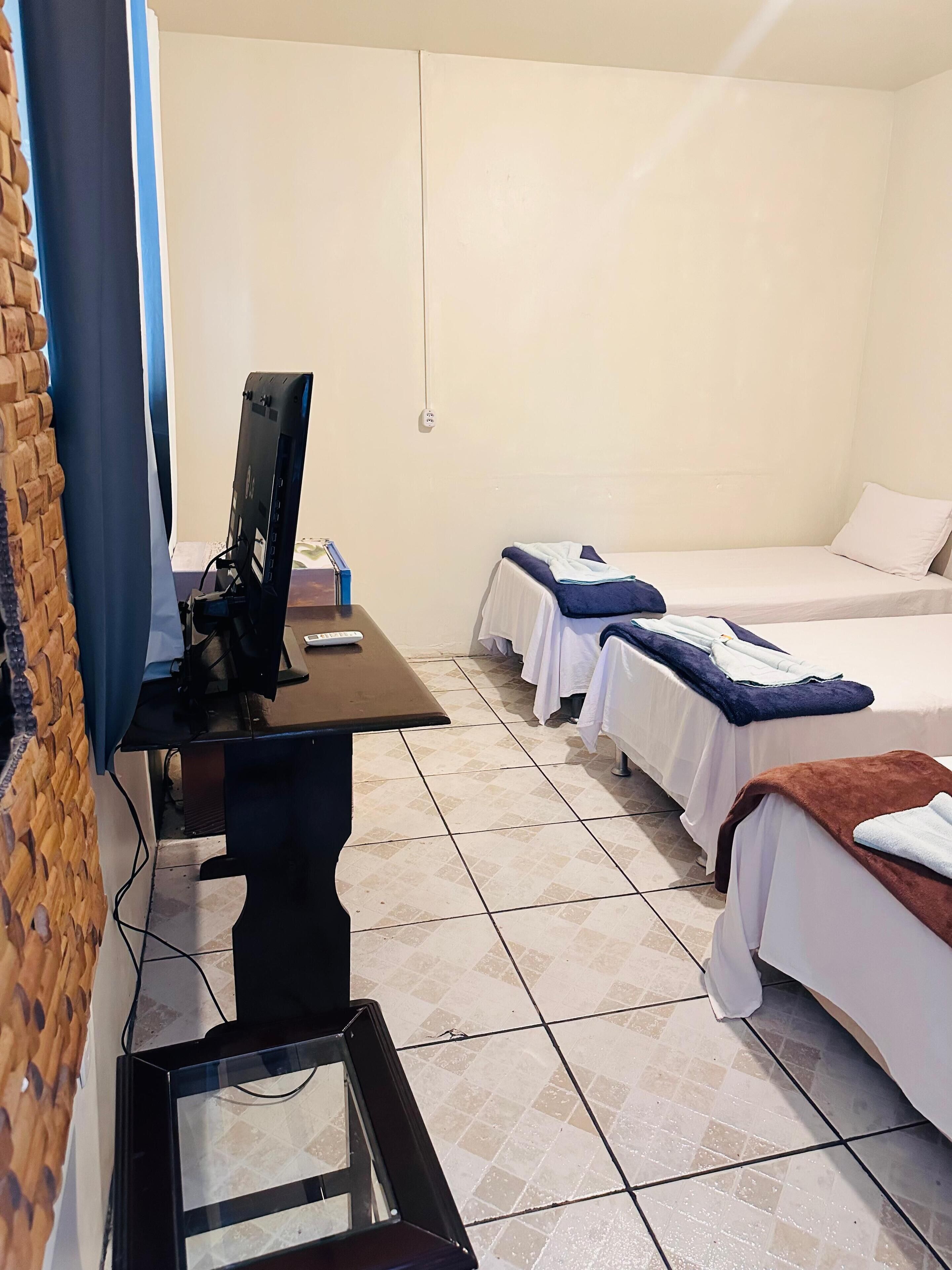 A hotel room with two single beds, a desk with a computer, and a tiled floor.