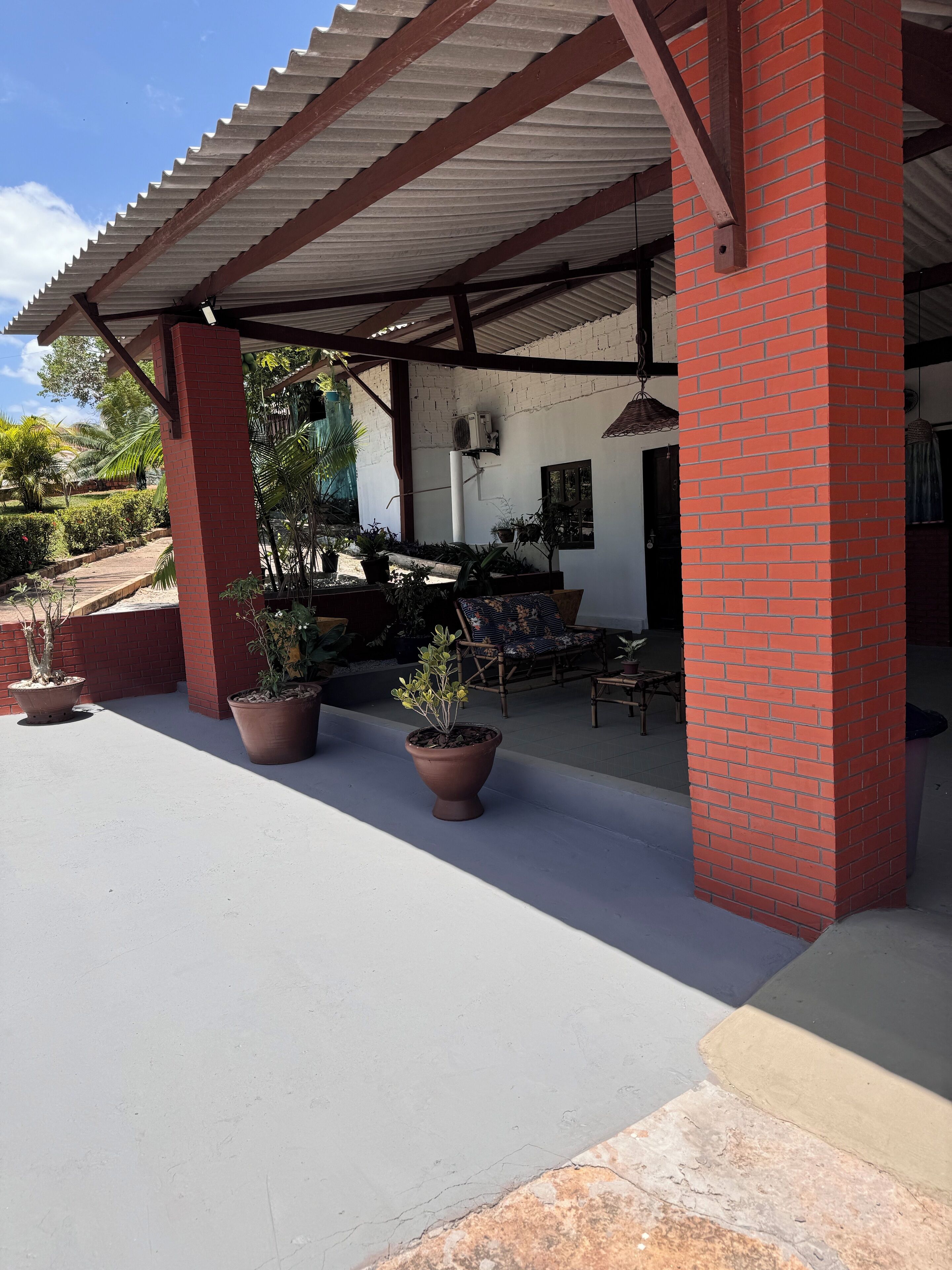 A covered outdoor area with brick pillars, potted plants, and a seating area with chairs and a table.