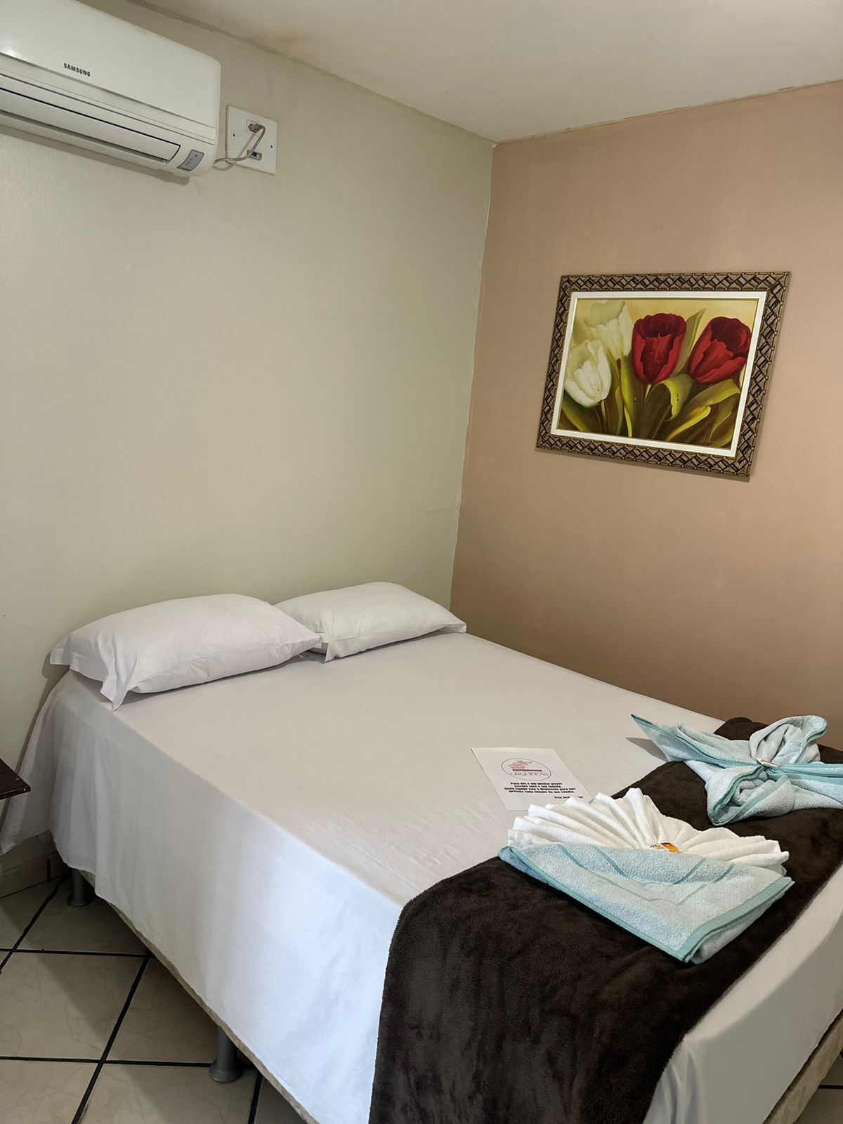 Ein Einzelbett mit weißer Bettwäsche, einer braunen Tagesdecke und einem Bilderrahmen mit Tulpen an der Wand.