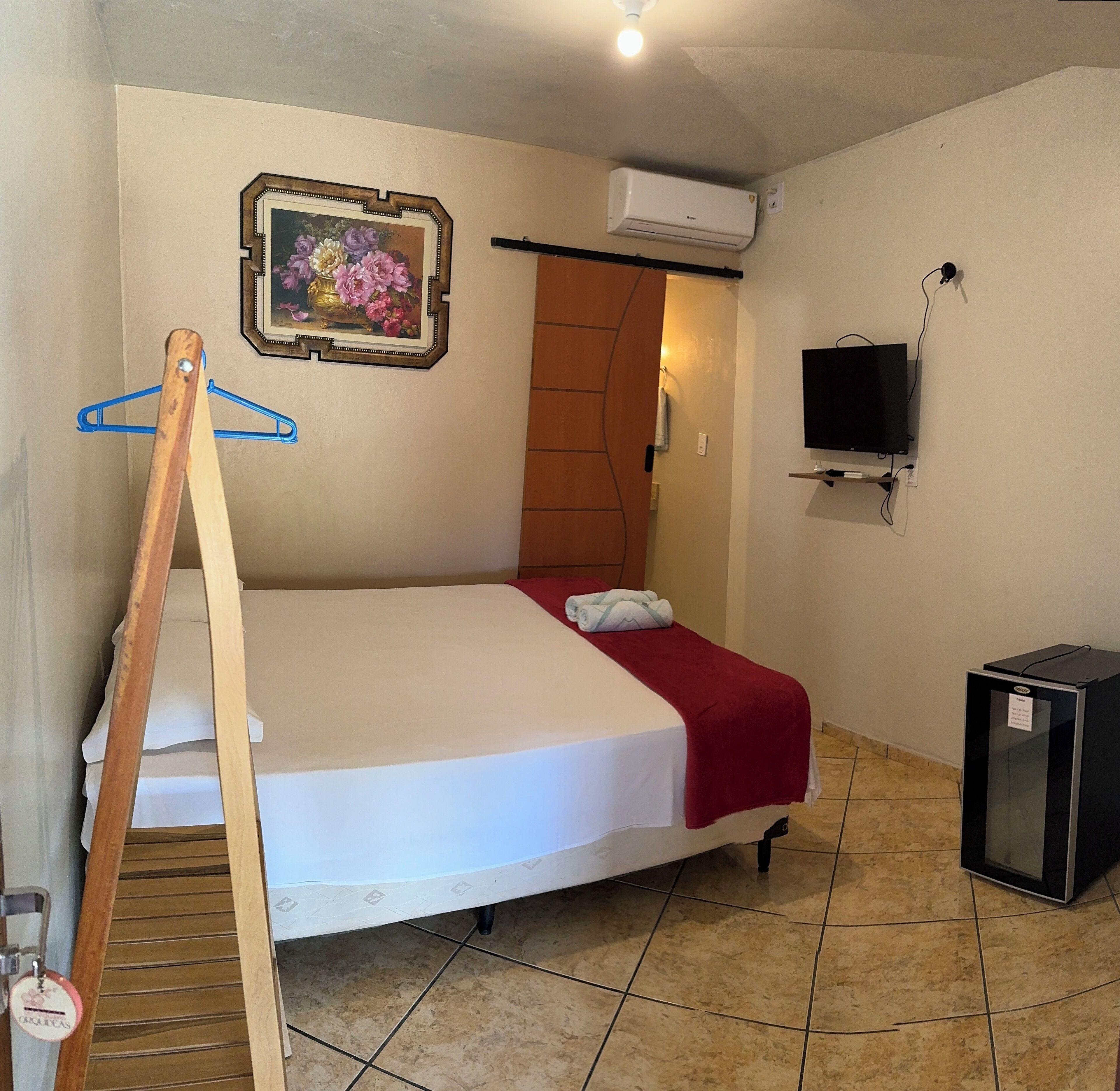 Ein Hotelzimmer mit Bett, Fernseher, Klimaanlage und einem Gemälde an der Wand.